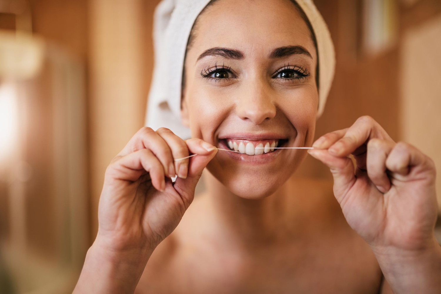 Mulher sorridente usando fio dental que se rompe nos dentes, um possível sinal de cárie tratado na Nakamura Odontologia em Barreiras - BA.