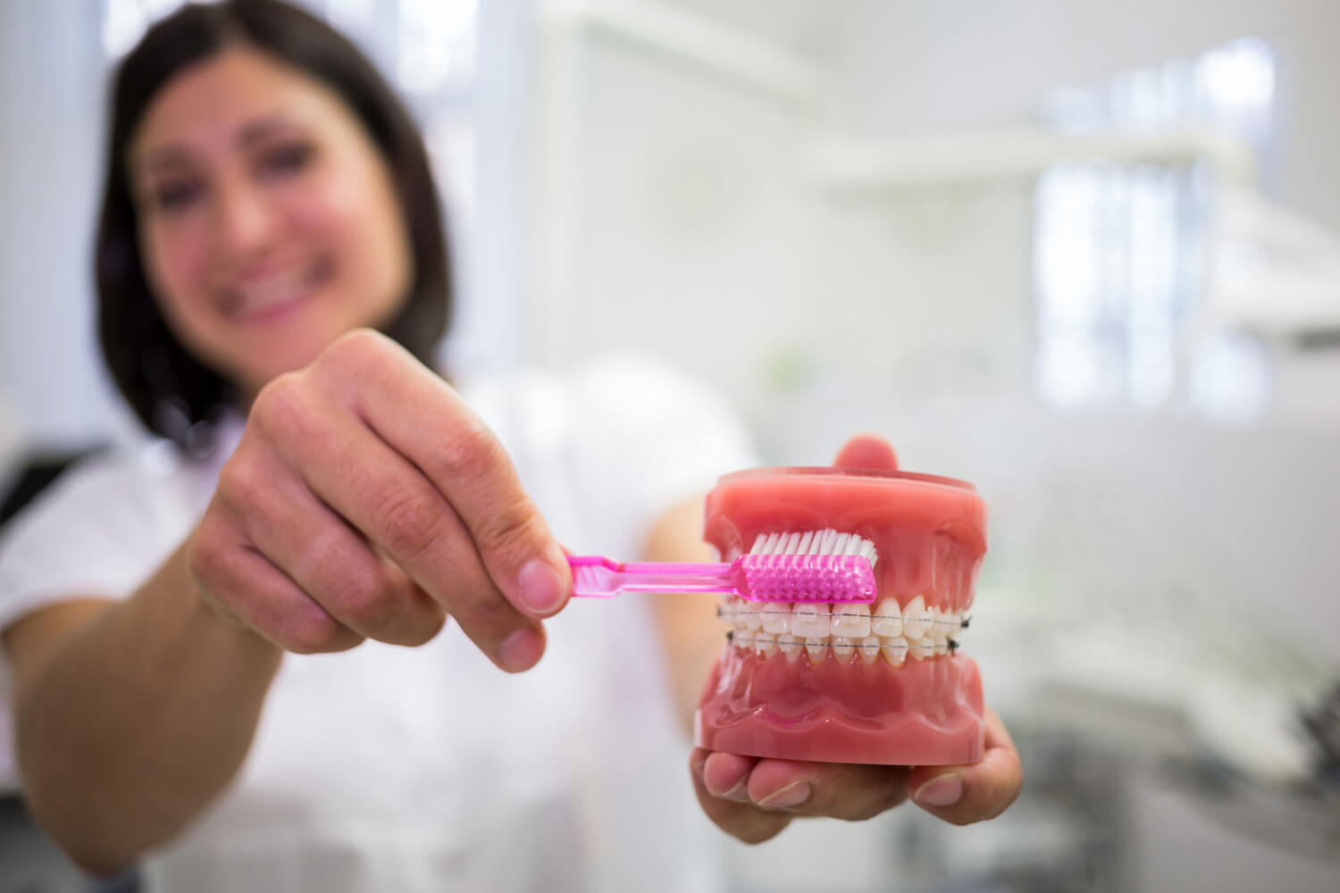 Dentista demonstrando a escovação em modelo dentário, essencial para prolongar a vida útil da sua prótese protocolo em Barreiras - BA.